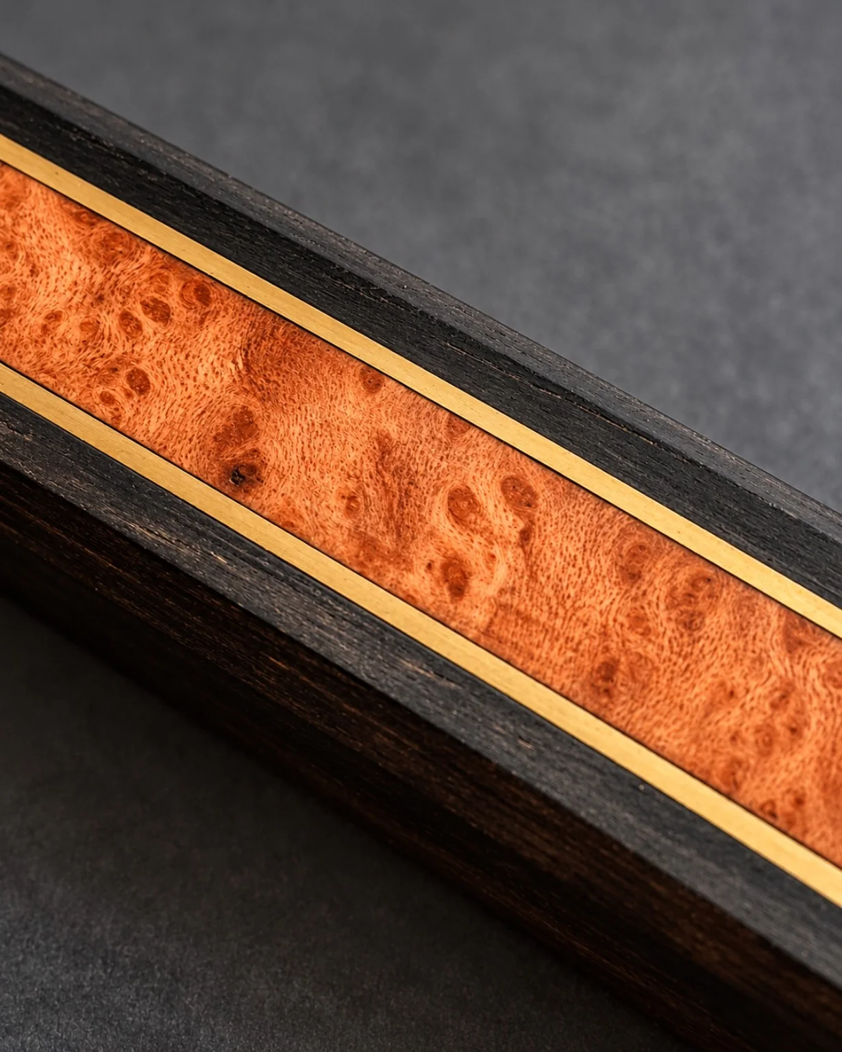 Macro view of an amber figured wood inlay enclosed by fine brass lines within a dark wood handle.