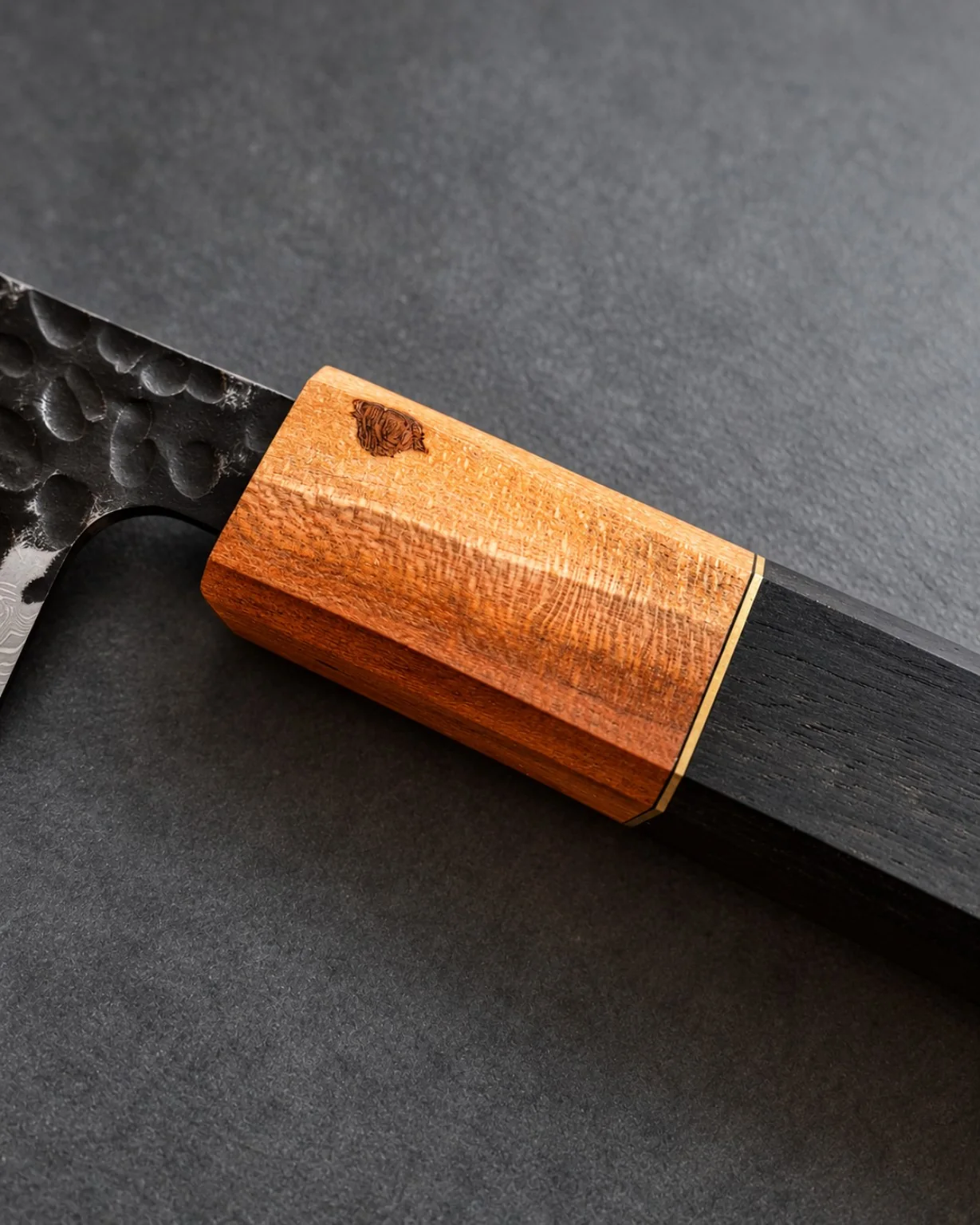 Detail of a figured reddish-gold wooden ferrule, brass spacer and dark knife handle.
